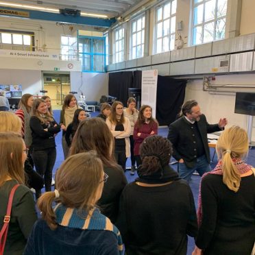 Eine kleine Gruppe Frauen steht um einen Mann herum, der ihnen etwas erklärt.