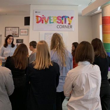eine Frau erzählt vor einer kleinen Gruppe junger Frauen. Im Hintergrund hängt ein Banner mit der bunten Aufschrift "Diversity Corner"