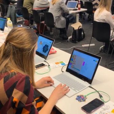 Eine Gruppe junger Frauen in einem Schulungsraum sitzt vor ihren Laptops und lauschen einem Vortrag.