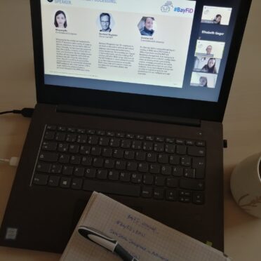 Laptop einer Workshop-Teilnehmerin zeigt eine Präsentationsfolie mit dem Profil von 3 Speakern - daneben ein Notizblock und eine Tasse Kaffee