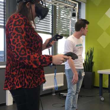 Eine Frau trägt eine Virtual Reality Brille und hält Steuerungsgeräte in den Händen.