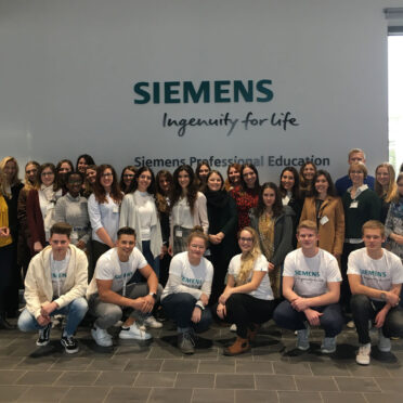 Gruppenbild der Teilnehmer*innen vor einer weißen Wand mit einem großen Siemens-Logo darauf.