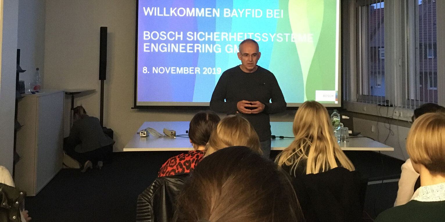 BayFiD Safari Tour – Vortrag Bosch Mann hält Vortrag vor einer kleinen Gruppe. Im Hintergrund ist eine Präsentation mit dem Hinweis auf Bosch Sicherheitssysteme zu sehen.