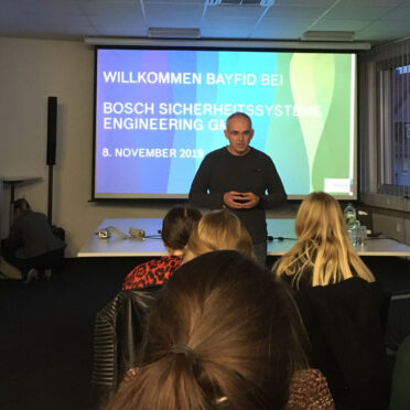 Mann hält Vortrag vor einer kleinen Gruppe. Im Hintergrund ist eine Präsentation mit dem Hinweis auf Bosch Sicherheitssysteme zu sehen.