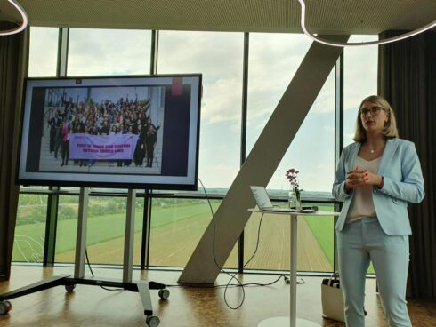 Ein BayFiD Talent hält einen Vortrag. Sie steht neben einem großen Bildschirm, der ein Gruppenbild der BayFiD Talente zeigt.